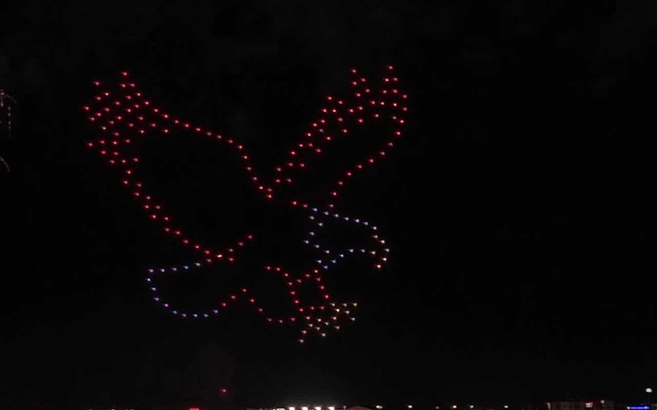 A drone light show forms an eagle with wings spread in red and blue against the night sky.