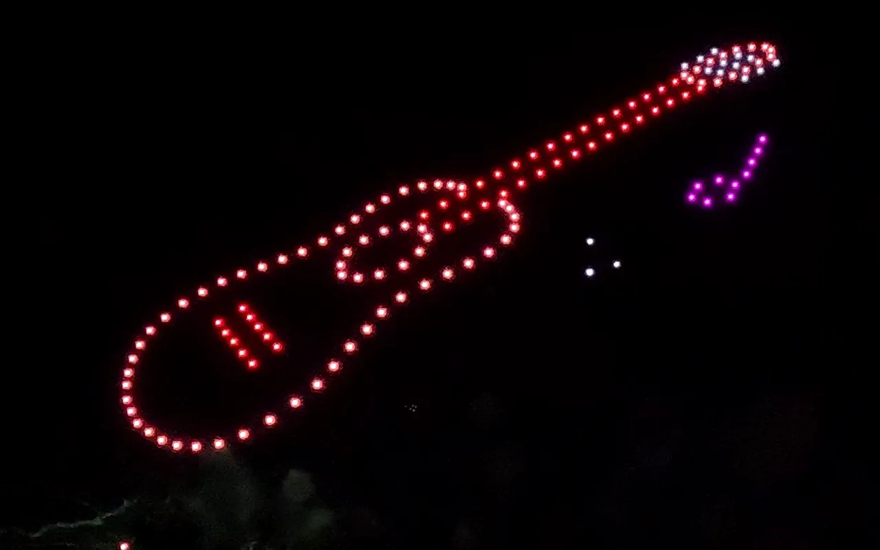 A drone light show forms a guitar outlined in red beside a music note. Immersion produces drone light shows in Austin, Texas.