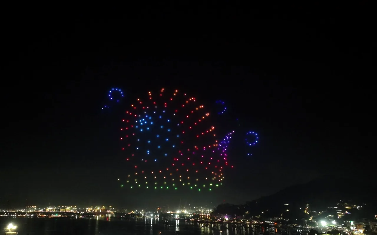 A drone light show forms a radiant burst in red, blue and green above a valley of lights. Immersion produces drone light shows in Boulder, Colorado.