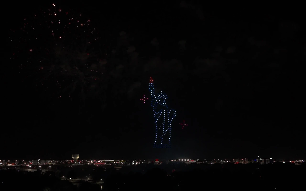 A drone light show forms the Statue of Liberty holding her torch, lit above the crowd at night.