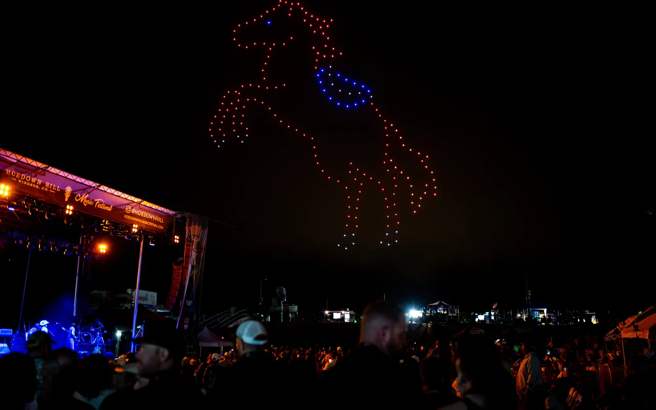 A drone light show forms a rearing horse above the crowd and the stage at night. Immersion produces drone light shows in Cheyenne, Wyoming.