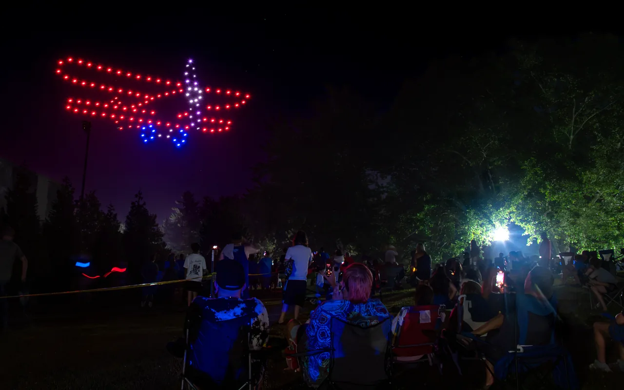 A drone light show forms an aircraft in red and blue above a standing crowd at night. Immersion produces drone light shows in Columbus, Ohio.
