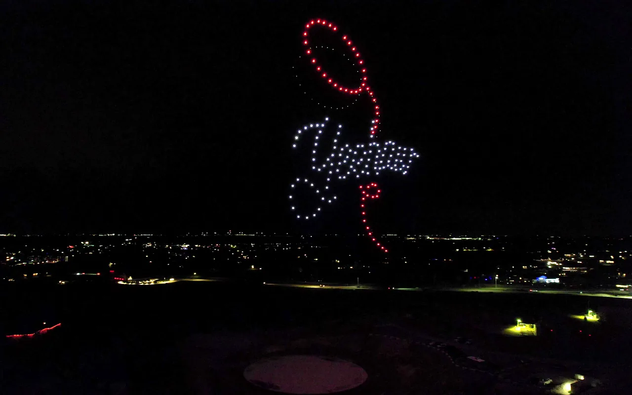 A drone light show forms flowing white script encircled by a red lasso above town lights. Immersion produces drone light shows in Dallas-Fort Worth, Texas.