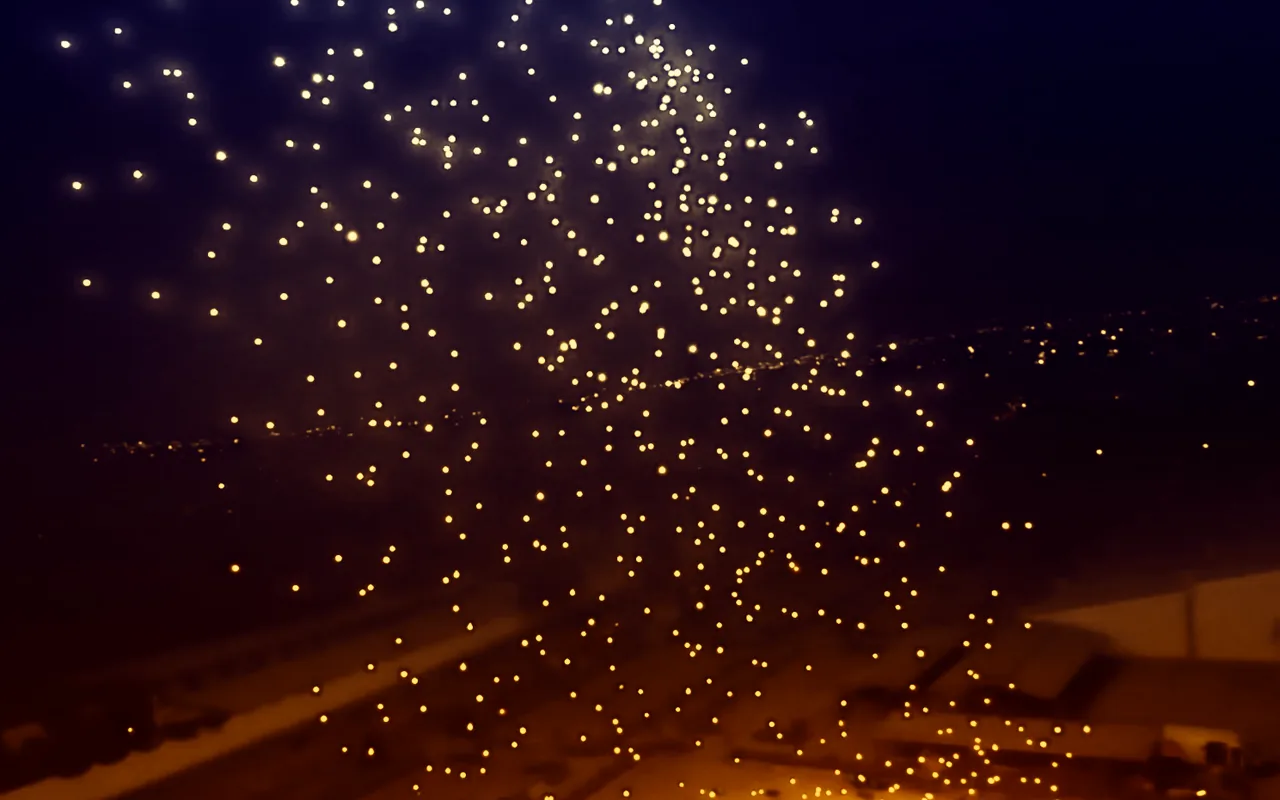A drone light show disperses into a wide gold burst above a lit city at night. Immersion produces drone light shows in Denver, Colorado.