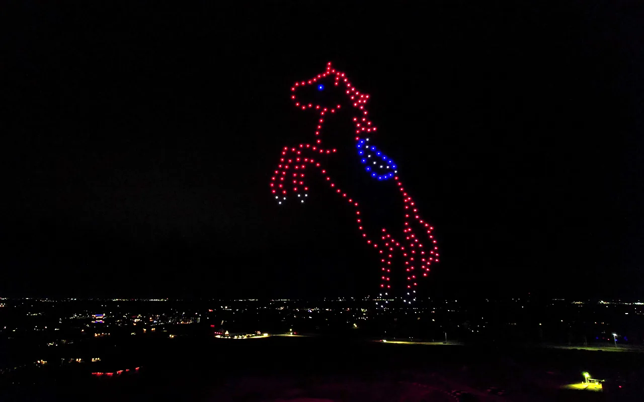 A drone light show forms a rearing horse above a valley of town lights at night. Immersion produces drone light shows in Greeley, Colorado.