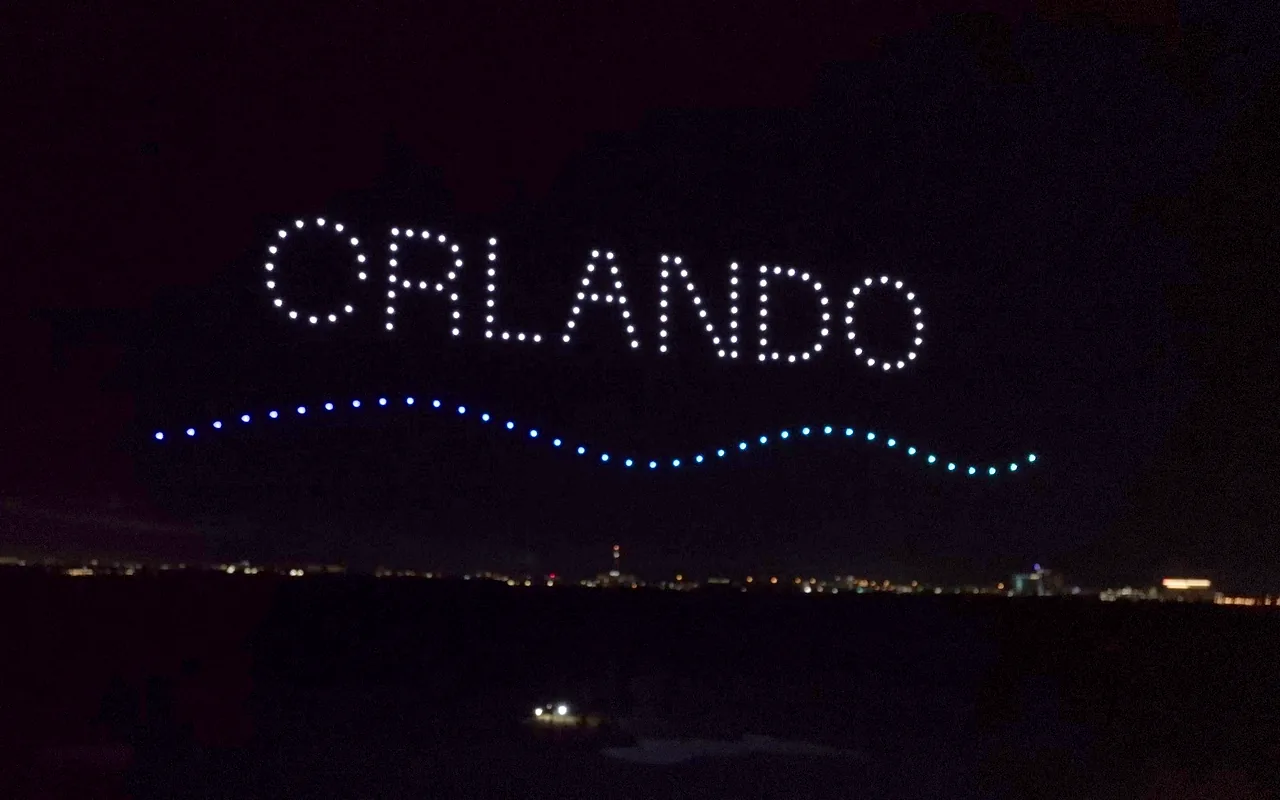 A drone light show spells ORLANDO in white letters above a curving blue wave at night. Immersion produces drone light shows in Orlando, Florida.