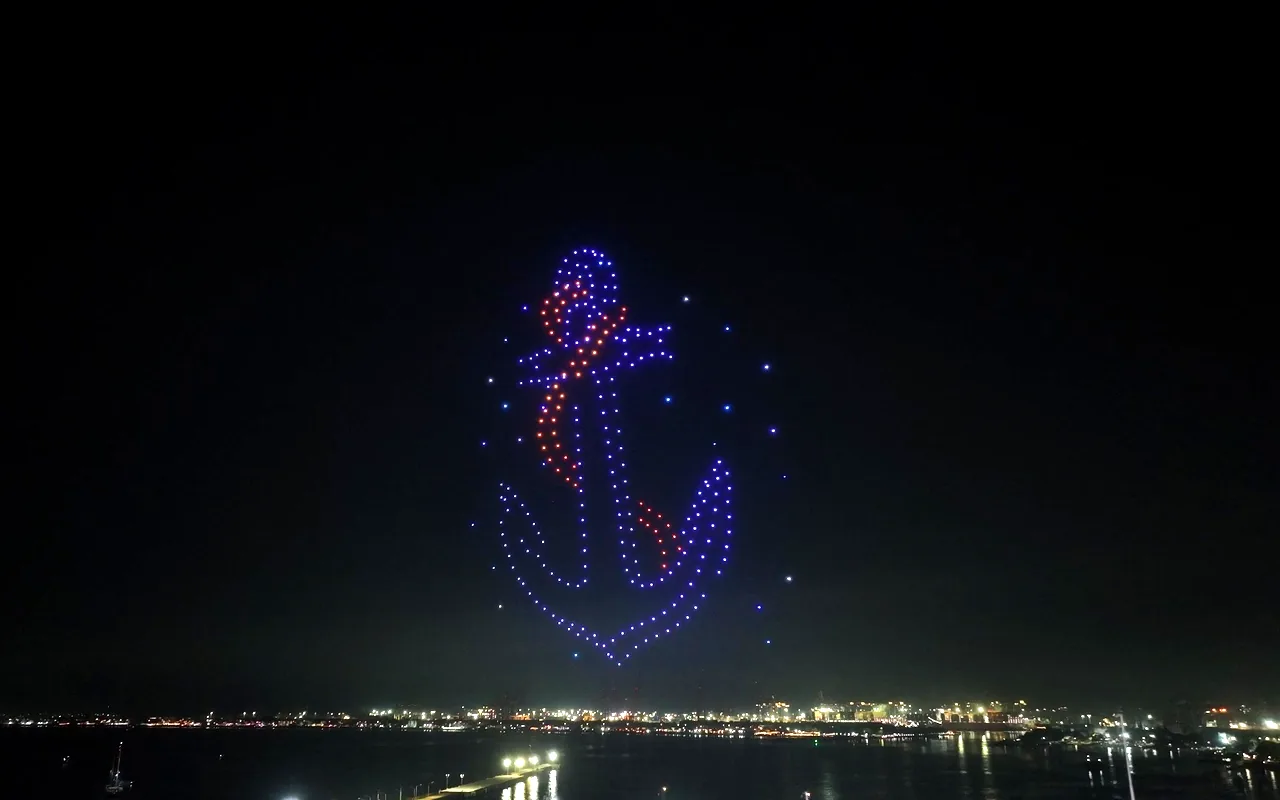 A drone light show forms a ship's anchor outlined in blue with a red rope above a harbor. Immersion produces drone light shows in Richmond, Virginia.