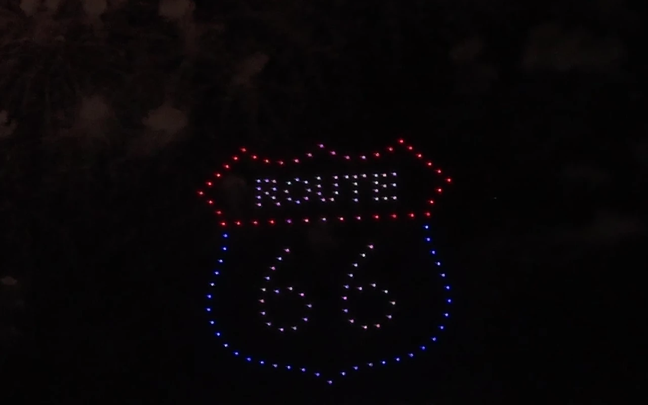 A drone light show forms a Route 66 shield reading 66 above a nighttime crowd.