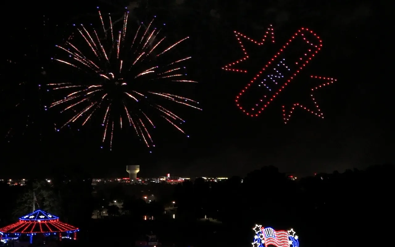 Fireworks burst beside a red, white, and blue drone formation over an Independence Day crowd, drones and fireworks in the same sky. Immersion produces drone light shows in Riverside, California.