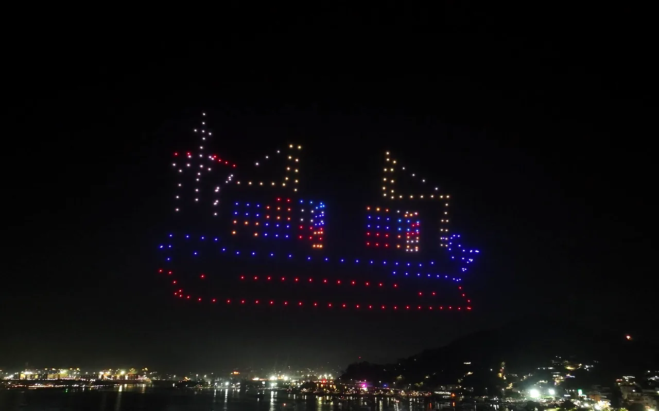 A drone light show forms a container ship in red, blue and orange above a harbor. Immersion produces drone light shows in Rochester, New York.