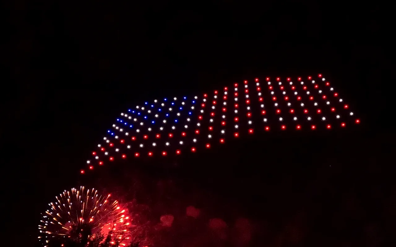 A drone light show forms an American flag waving above fireworks at night. Immersion produces drone light shows in Steamboat Springs, Colorado.