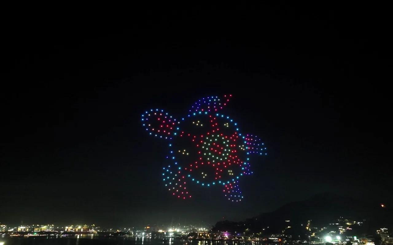A drone light show forms a sea turtle in green, red and blue above a bay at night. Immersion produces drone light shows in Tampa, Florida.