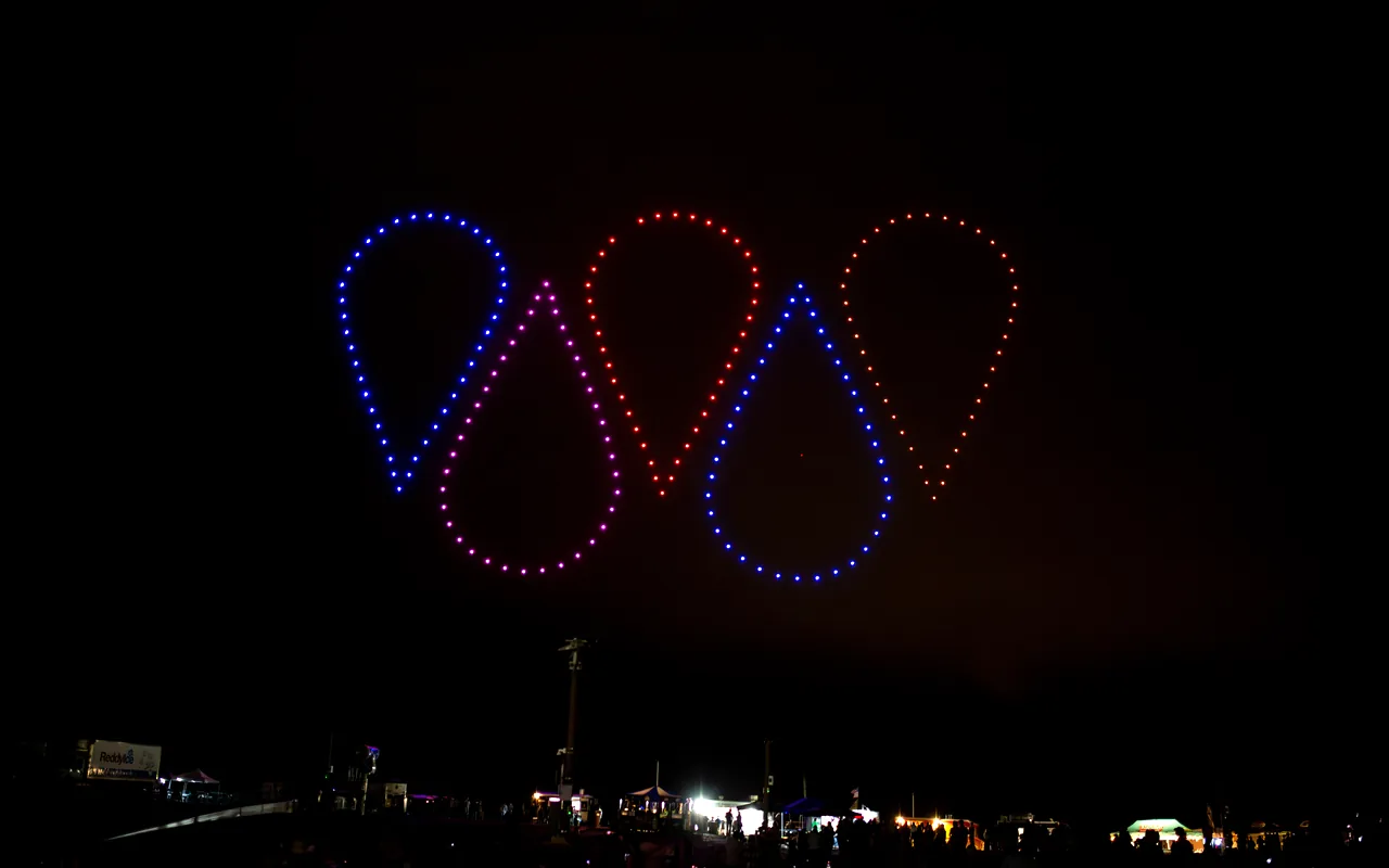 A drone light show forms glowing shapes in red and blue above the town at night. Immersion produces drone light shows in Windsor, Colorado.